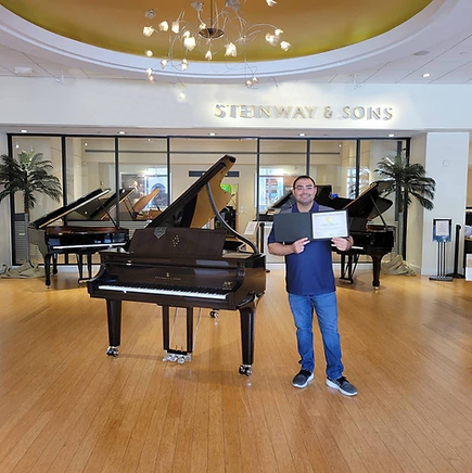 Piano instructor in Fort Myers holding a music certificate beside a grand piano, highlighting professionalism and accredited piano lessons